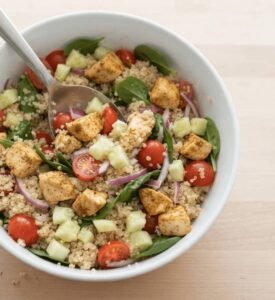 Quinoa recipe with chicken featuring fresh tomatoes, cucumber and spinach